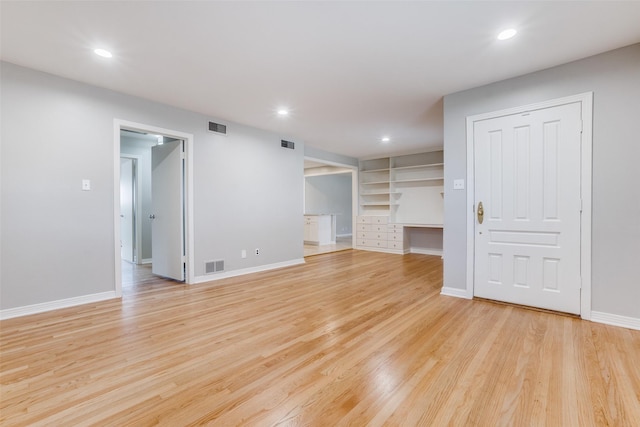 unfurnished living room featuring light hardwood / wood-style floors, built in features, and built in desk