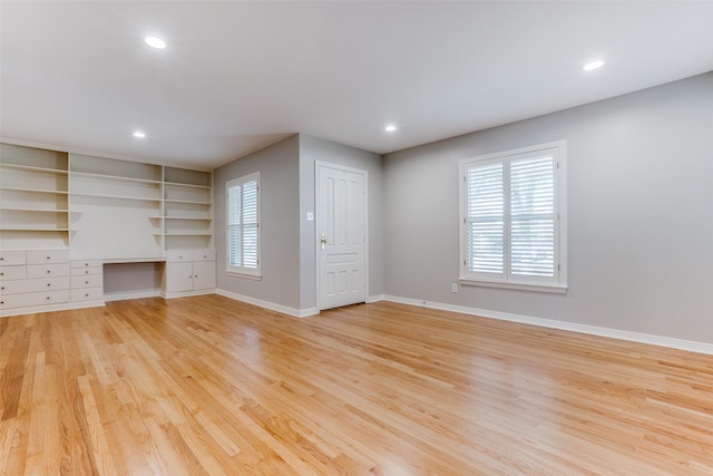 unfurnished living room featuring light hardwood / wood-style floors, built in features, and built in desk