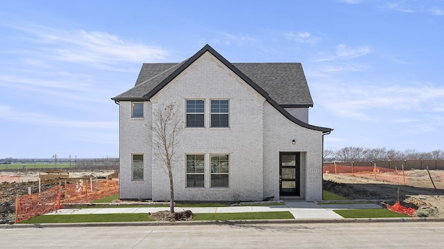 view of front of home featuring roof with shingles, fence, and brick siding