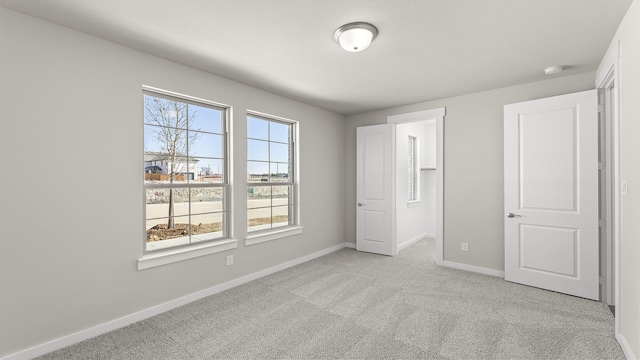 unfurnished bedroom featuring a walk in closet, light colored carpet, and baseboards