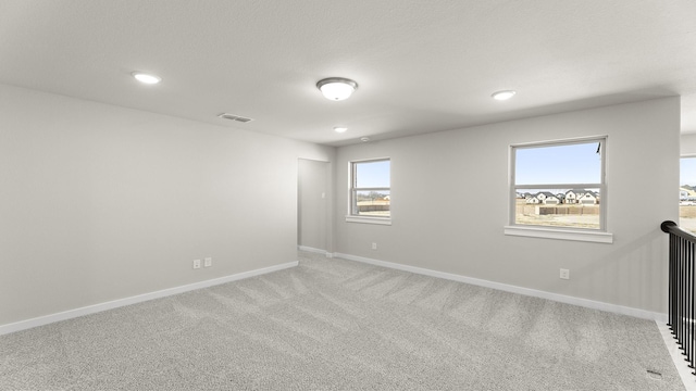 spare room featuring a wealth of natural light, carpet flooring, visible vents, and baseboards