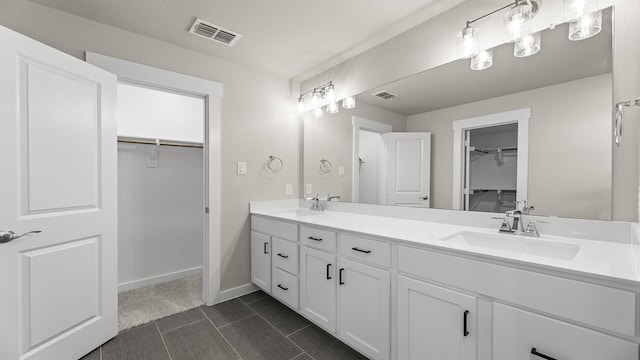 full bath with double vanity, visible vents, a walk in closet, and a sink