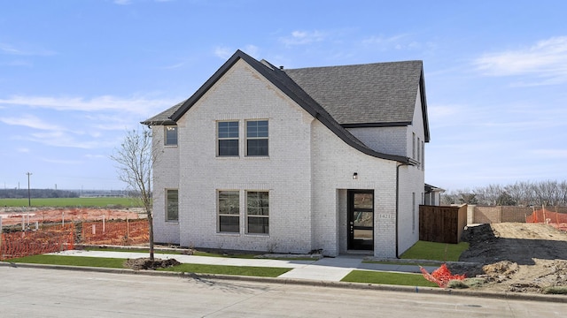 view of front of home with a shingled roof, brick siding, and fence