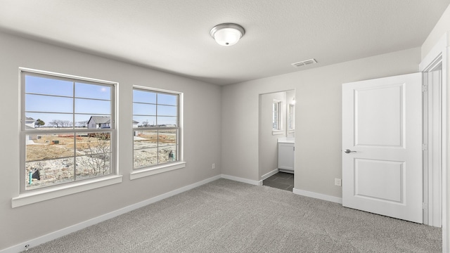 unfurnished bedroom with visible vents, baseboards, connected bathroom, carpet, and a textured ceiling