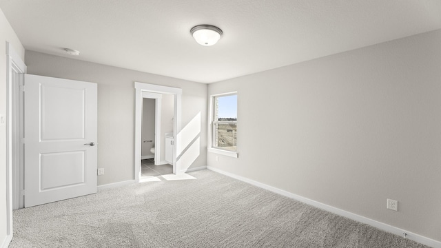 unfurnished bedroom featuring light carpet, ensuite bath, and baseboards