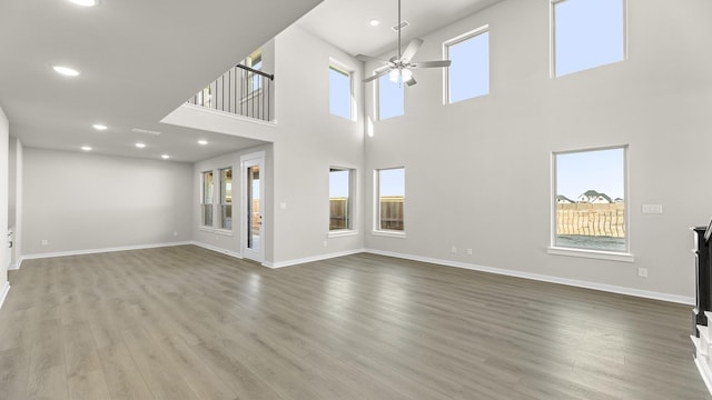 unfurnished living room featuring plenty of natural light, baseboards, a ceiling fan, and wood finished floors