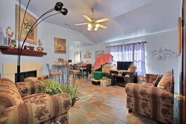 living room with ceiling fan, vaulted ceiling, and a tiled fireplace