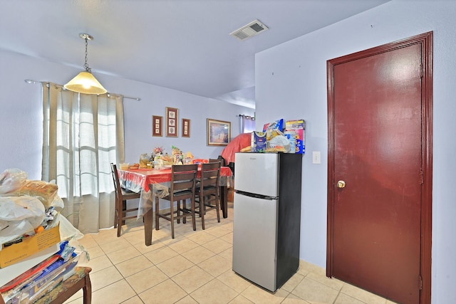 kitchen with light tile patterned floors, hanging light fixtures, and stainless steel refrigerator