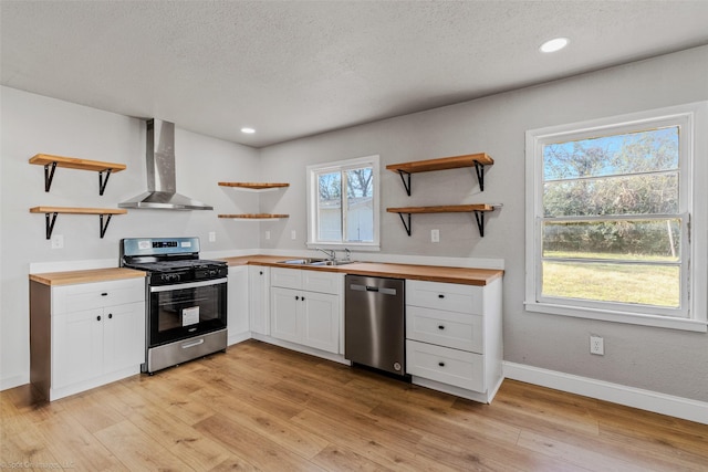 kitchen with white cabinets, appliances with stainless steel finishes, wall chimney range hood, butcher block counters, and sink