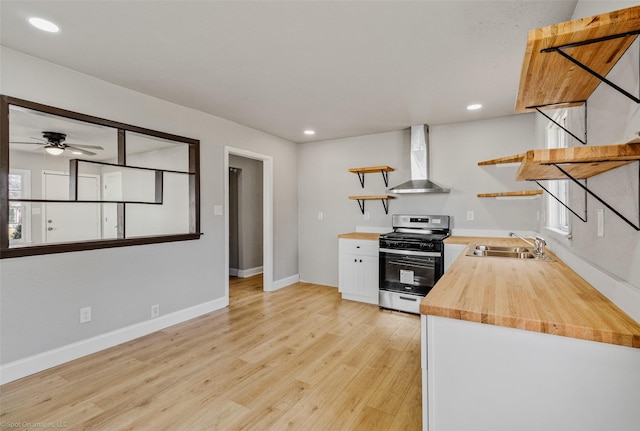 kitchen featuring wood counters, white cabinetry, wall chimney range hood, sink, and stainless steel range with gas cooktop