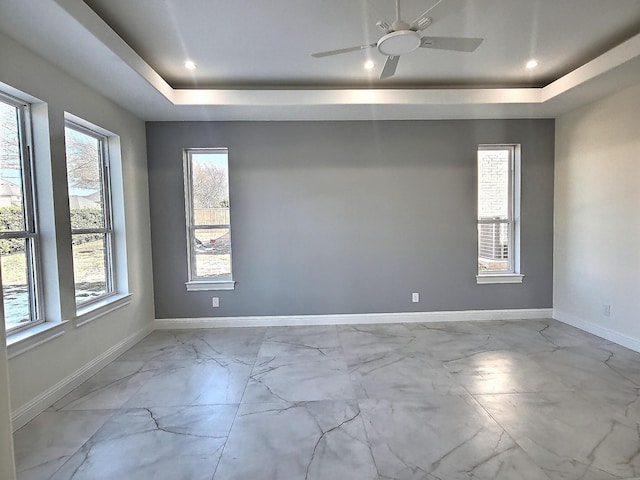 empty room featuring ceiling fan, plenty of natural light, and a tray ceiling