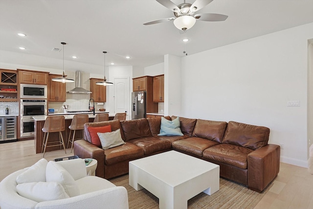 living room with beverage cooler, ceiling fan, and light hardwood / wood-style flooring