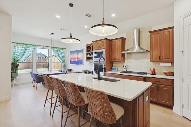 kitchen featuring built in microwave, stainless steel gas stovetop, an island with sink, and wall chimney exhaust hood