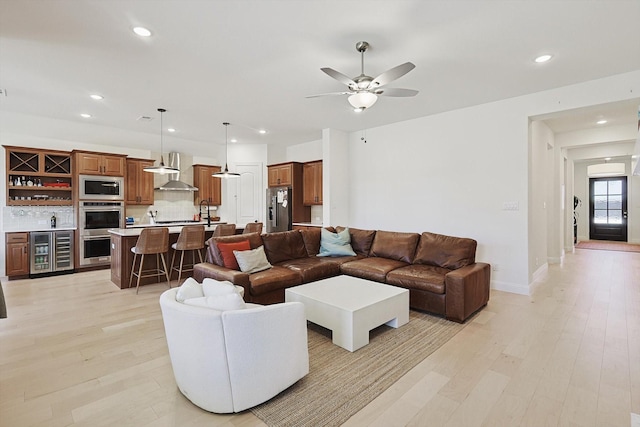 living room with bar, beverage cooler, ceiling fan, and light wood-type flooring