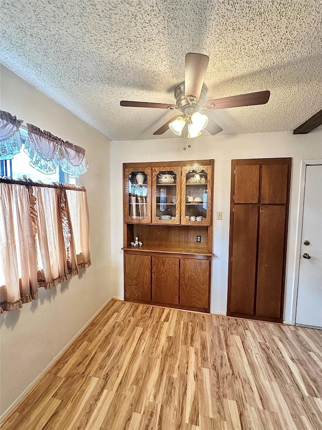 unfurnished dining area with light wood-type flooring, ceiling fan, and a textured ceiling