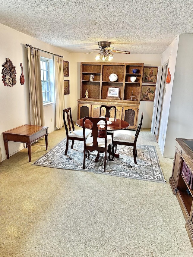 dining area featuring light carpet, ceiling fan, and a textured ceiling