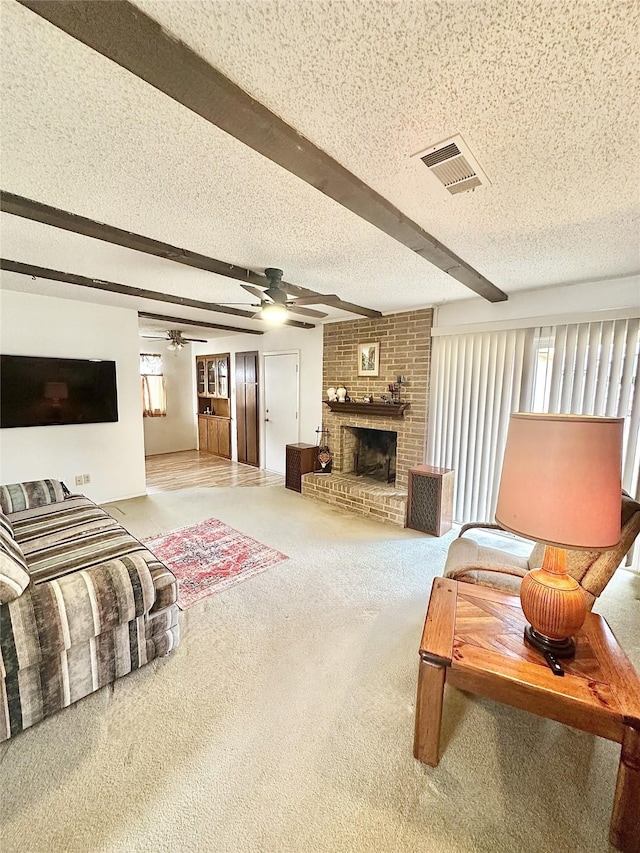 carpeted living room with a textured ceiling, a fireplace, beam ceiling, and ceiling fan