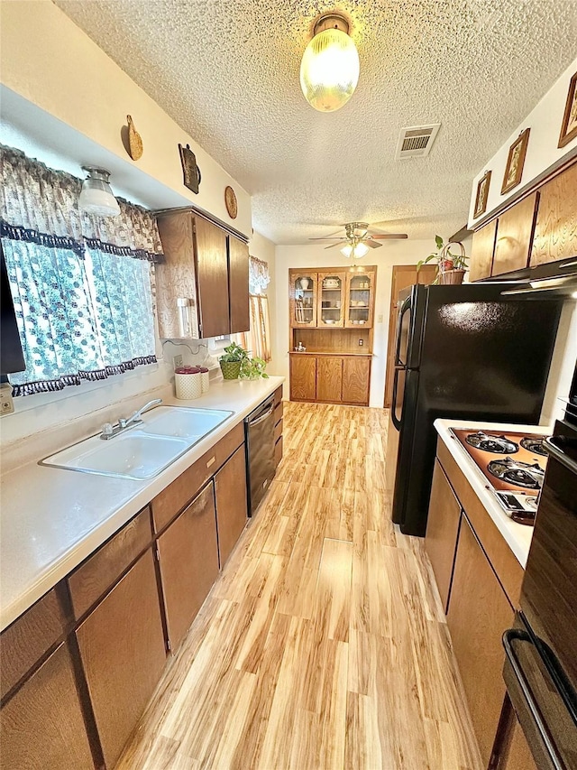 kitchen with a textured ceiling, dishwasher, sink, cooktop, and light hardwood / wood-style flooring