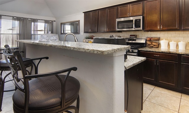 kitchen featuring a kitchen breakfast bar, stainless steel appliances, lofted ceiling, and a kitchen island with sink