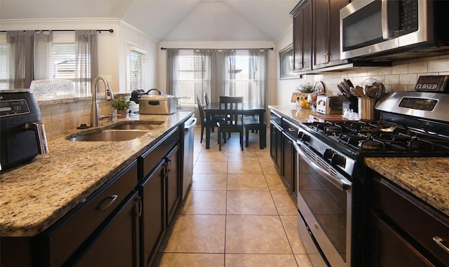 kitchen with light stone countertops, appliances with stainless steel finishes, sink, vaulted ceiling, and light tile patterned floors