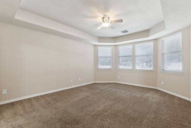 carpeted spare room with ceiling fan, plenty of natural light, and a tray ceiling