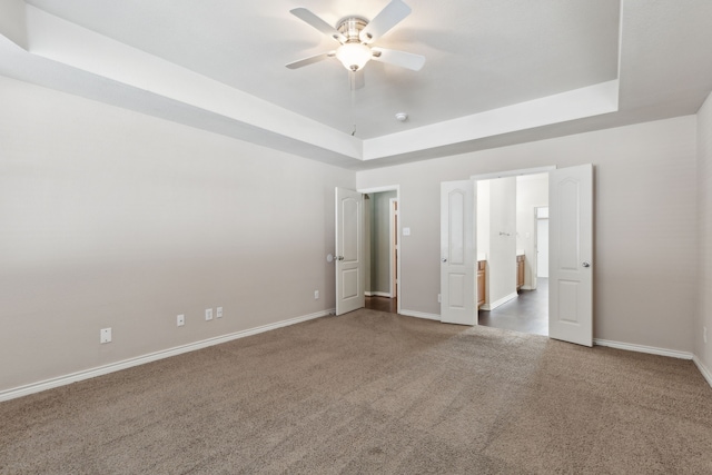 unfurnished bedroom with ceiling fan, a tray ceiling, and carpet flooring