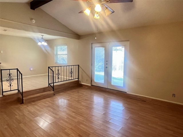 empty room featuring vaulted ceiling with beams, wood-type flooring, ceiling fan with notable chandelier, and french doors