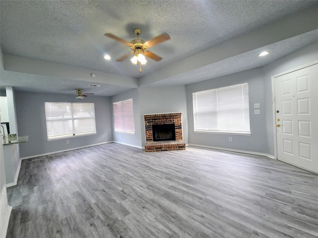 unfurnished living room featuring wood-type flooring, a fireplace, a textured ceiling, and ceiling fan