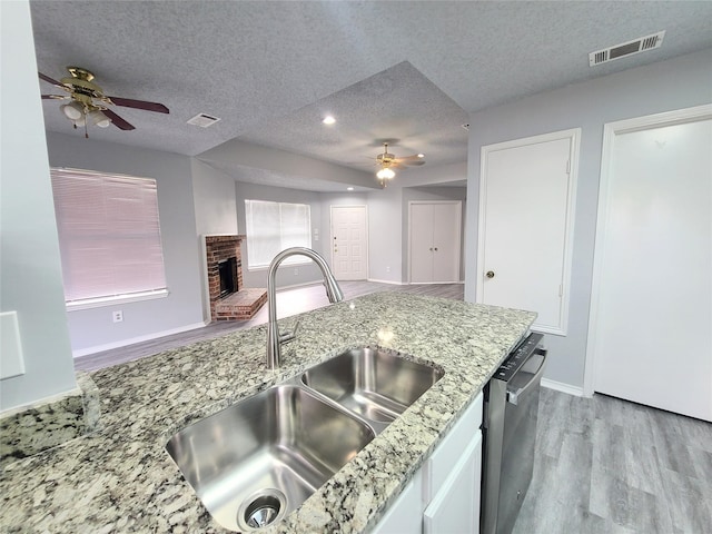 kitchen featuring white cabinetry, sink, stainless steel dishwasher, a brick fireplace, and a textured ceiling