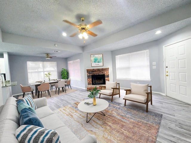 living room with ceiling fan, a fireplace, a textured ceiling, and light wood-type flooring