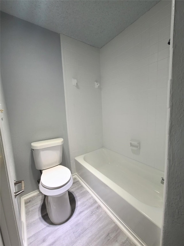 bathroom featuring tiled shower, wood-type flooring, toilet, and a textured ceiling