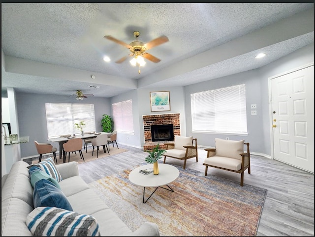 living room with ceiling fan, a textured ceiling, a fireplace, and light wood-type flooring