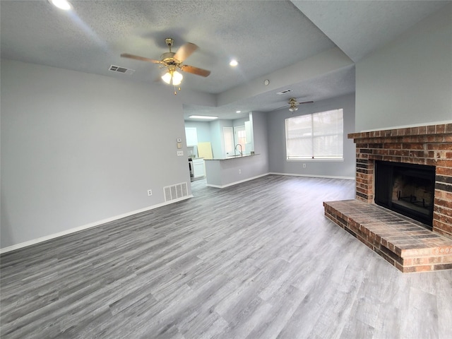 unfurnished living room with wood-type flooring, ceiling fan, a fireplace, and a textured ceiling