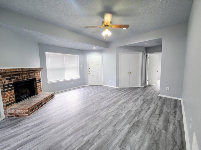 unfurnished living room with ceiling fan, a fireplace, a textured ceiling, and light hardwood / wood-style floors