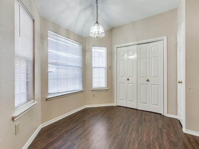 unfurnished bedroom with a textured ceiling, dark wood-type flooring, an inviting chandelier, and multiple windows