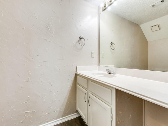 bathroom with a textured ceiling, vanity, and vaulted ceiling