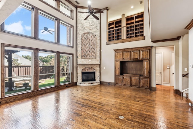 unfurnished living room featuring dark wood-type flooring, ceiling fan, a high ceiling, and a stone fireplace