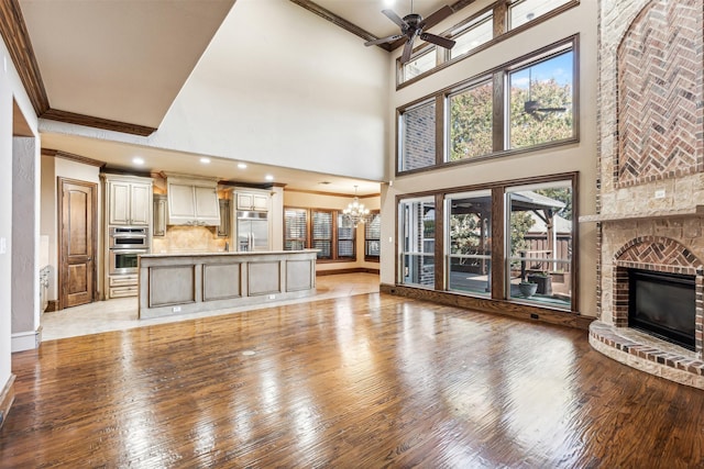 unfurnished living room featuring ceiling fan with notable chandelier, a high ceiling, a fireplace, light hardwood / wood-style floors, and ornamental molding