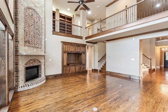 living room with a brick fireplace, wood-type flooring, ceiling fan with notable chandelier, and a high ceiling