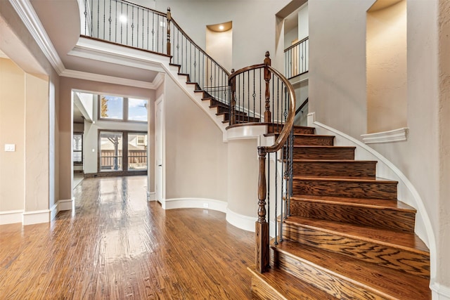 stairs featuring hardwood / wood-style floors, crown molding, and a high ceiling