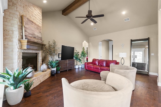 living room featuring ceiling fan, dark hardwood / wood-style floors, beamed ceiling, and a stone fireplace