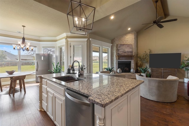 kitchen with pendant lighting, stainless steel appliances, sink, light stone counters, and a center island with sink