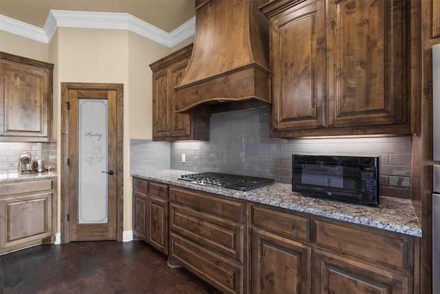 kitchen featuring wall chimney range hood, dark brown cabinetry, stainless steel gas cooktop, light stone countertops, and dark hardwood / wood-style flooring