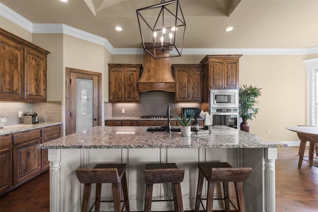 kitchen with appliances with stainless steel finishes, dark hardwood / wood-style floors, a kitchen island with sink, light stone counters, and crown molding