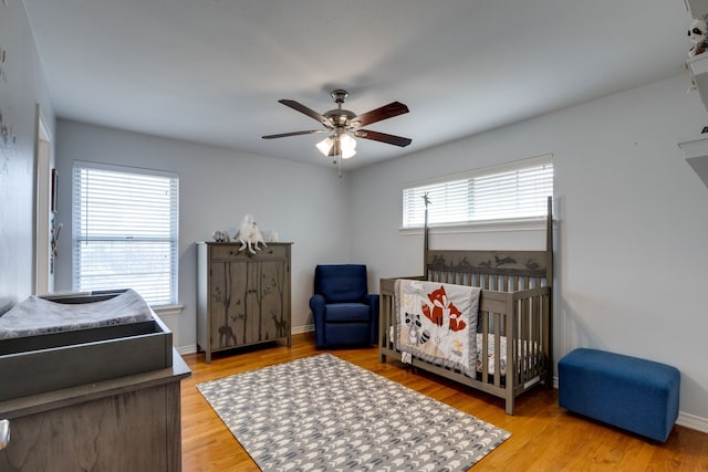 bedroom with a crib, multiple windows, light hardwood / wood-style flooring, and ceiling fan