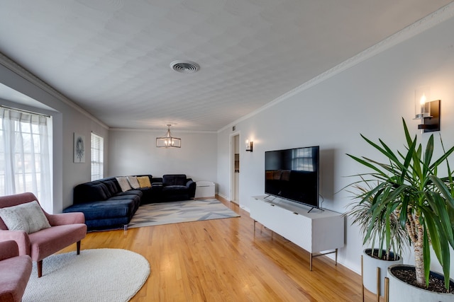 living room featuring an inviting chandelier, ornamental molding, and light wood-type flooring