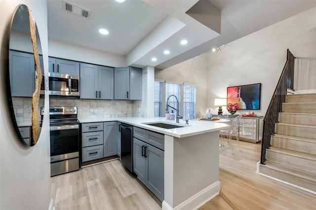 kitchen with kitchen peninsula, appliances with stainless steel finishes, sink, and light hardwood / wood-style floors