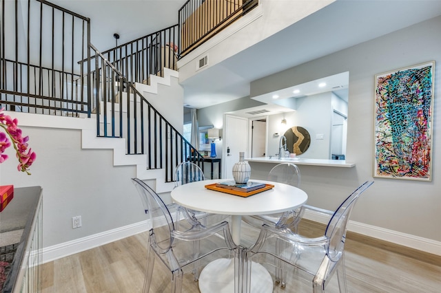 dining space featuring light wood-type flooring, a towering ceiling, and sink