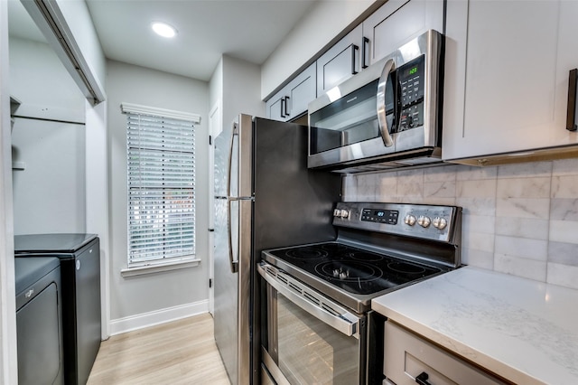 kitchen featuring backsplash, light hardwood / wood-style flooring, washer and clothes dryer, gray cabinetry, and stainless steel appliances