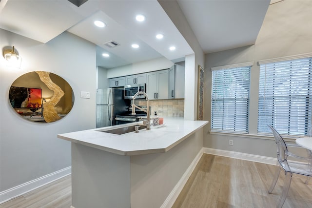 kitchen featuring stainless steel appliances, decorative backsplash, light hardwood / wood-style flooring, and kitchen peninsula